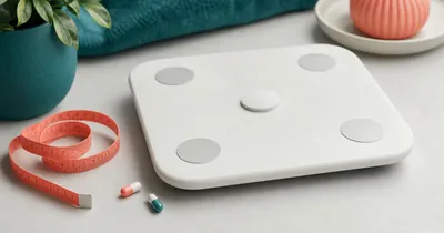 Pastillas para Bajar de Peso: Qué Son, Cómo Funcionan y Cómo Usarlas Bien White bathroom scale with a coral measuring tape and two capsules