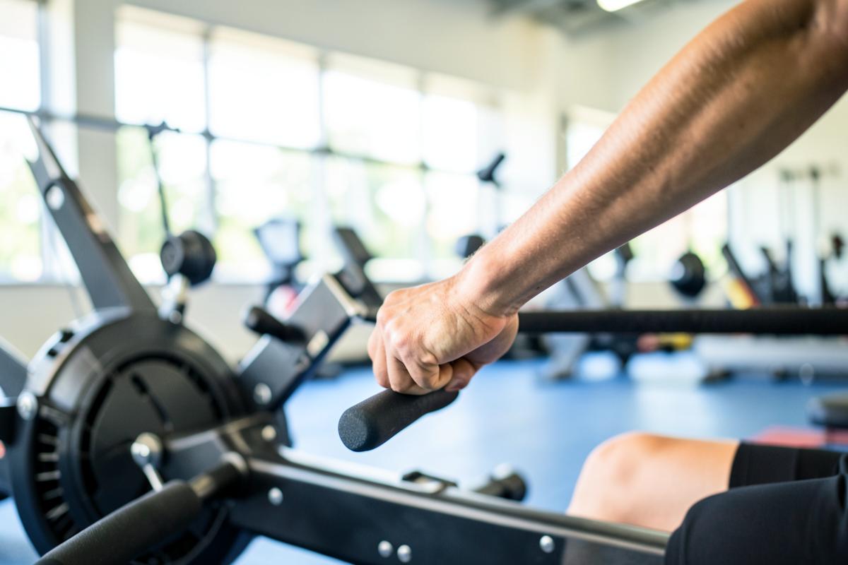 An athlete's forearm mid-effort on a rowing machine in a bright gym