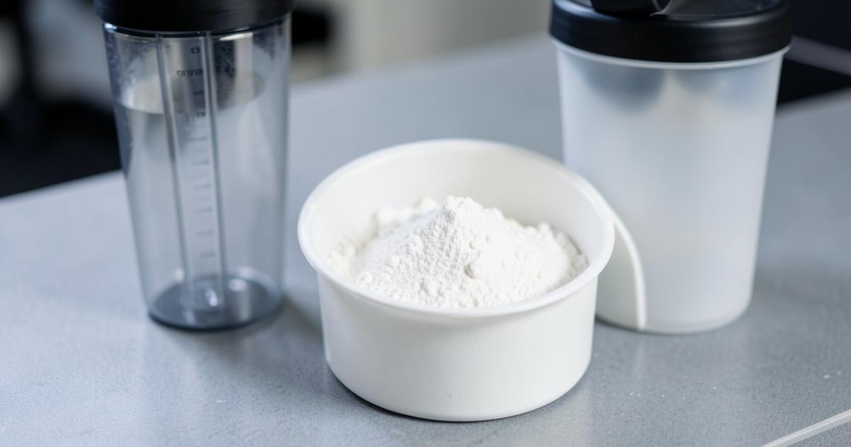 A scoop of creatine monohydrate powder over an open tub beside a shaker bottle
