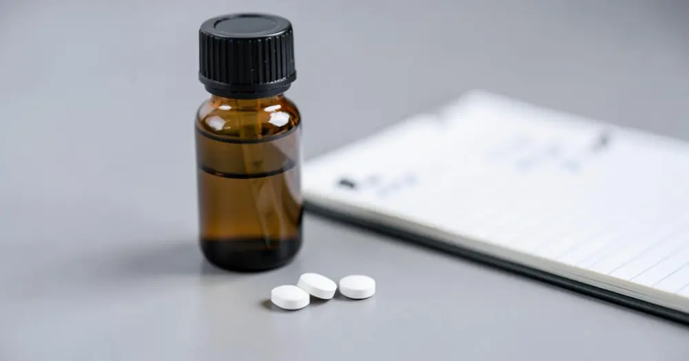 Amber supplement bottle and white tablets on a grey surface beside a lab notebook Amber supplement bottle and white tablets on a grey surface beside a lab notebook