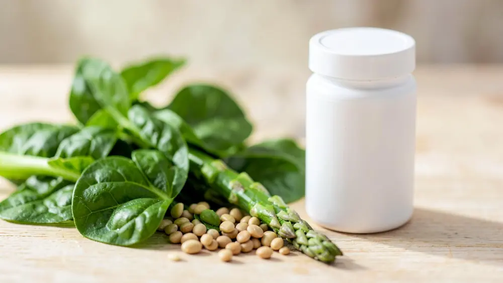 Spinach leaves, lentils and asparagus on a wooden table beside a plain white pill bottle Spinach leaves, lentils and asparagus on a wooden table beside a plain white pill bottle