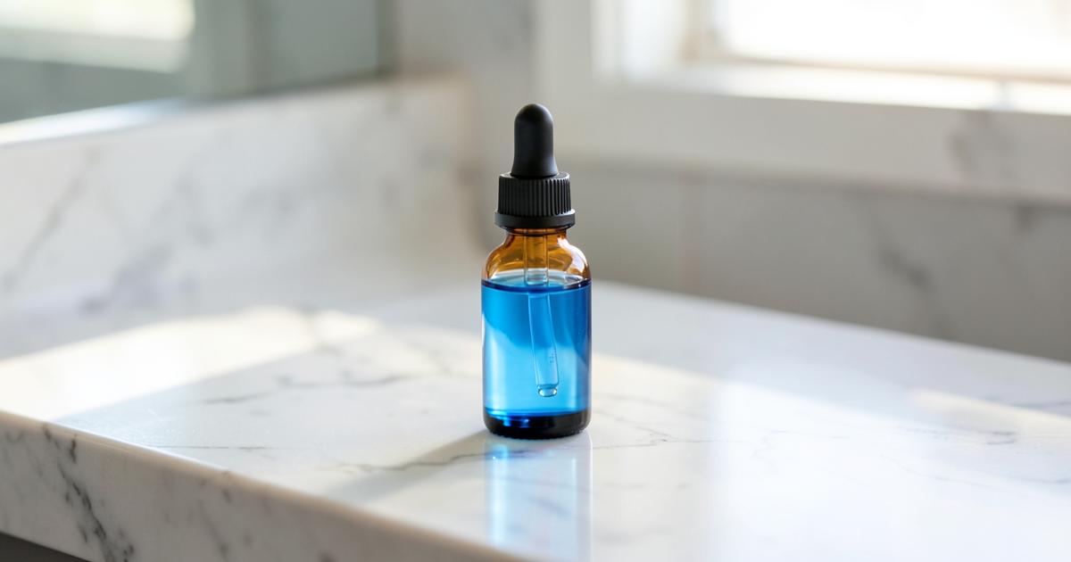 An amber dropper bottle of blue serum on a marble bathroom counter