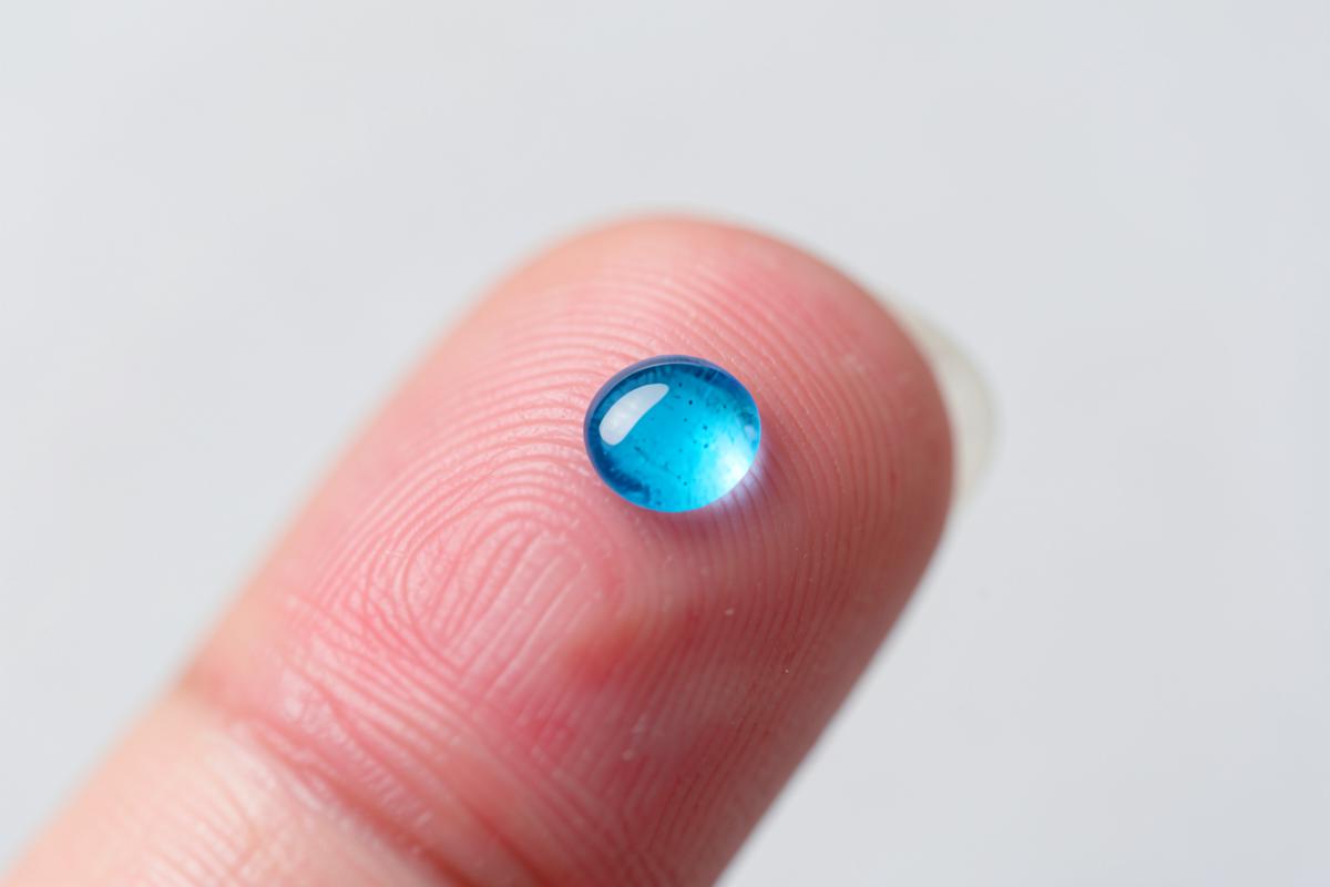 A drop of blue serum on a fingertip, close up