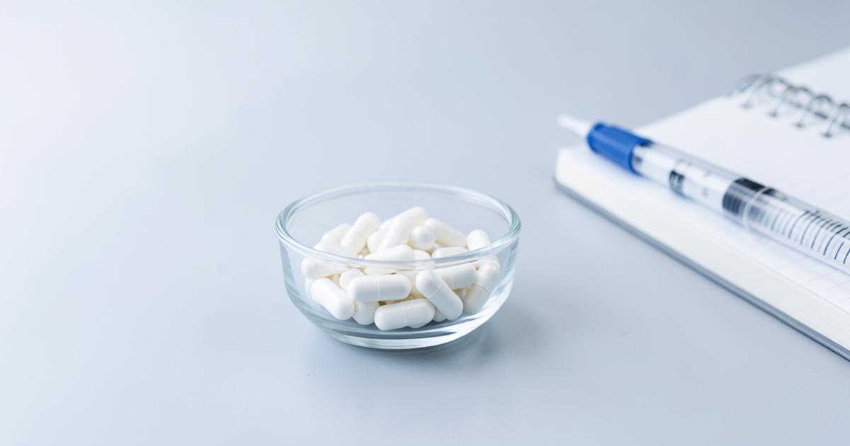 White capsules in a small glass dish on a laboratory bench beside a pipette and notebook