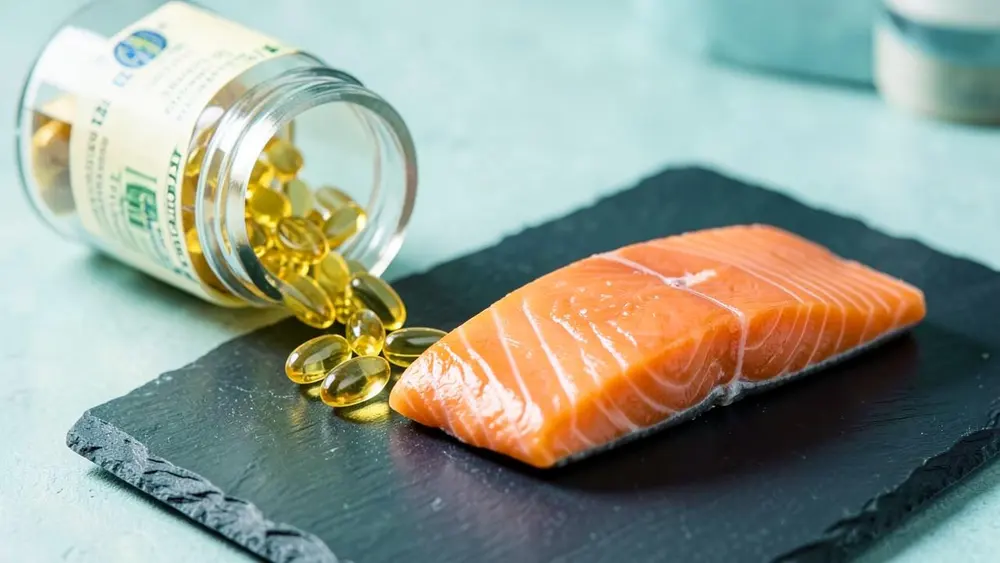 Golden fish oil capsules spilling from a bottle beside a fresh salmon fillet Golden fish oil capsules spilling from a bottle beside a fresh salmon fillet