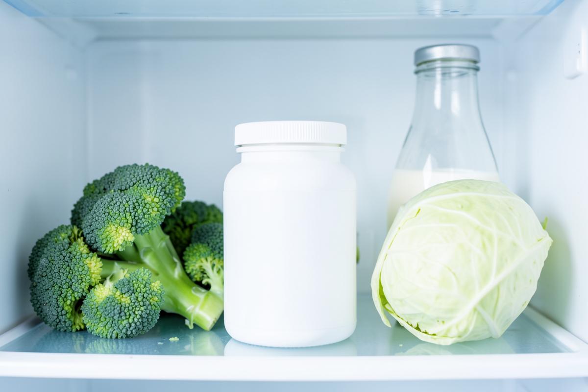 A probiotic supplement bottle stored on a refrigerator shelf beside fresh food