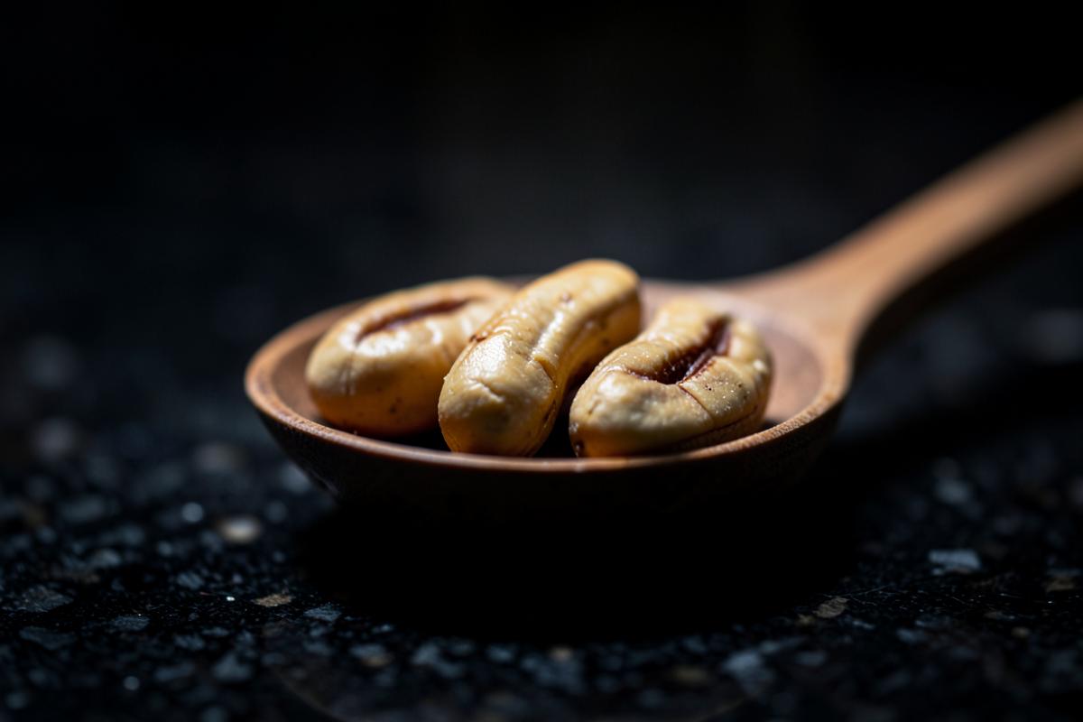 Three brazil nuts in a small wooden spoon on a dark counter