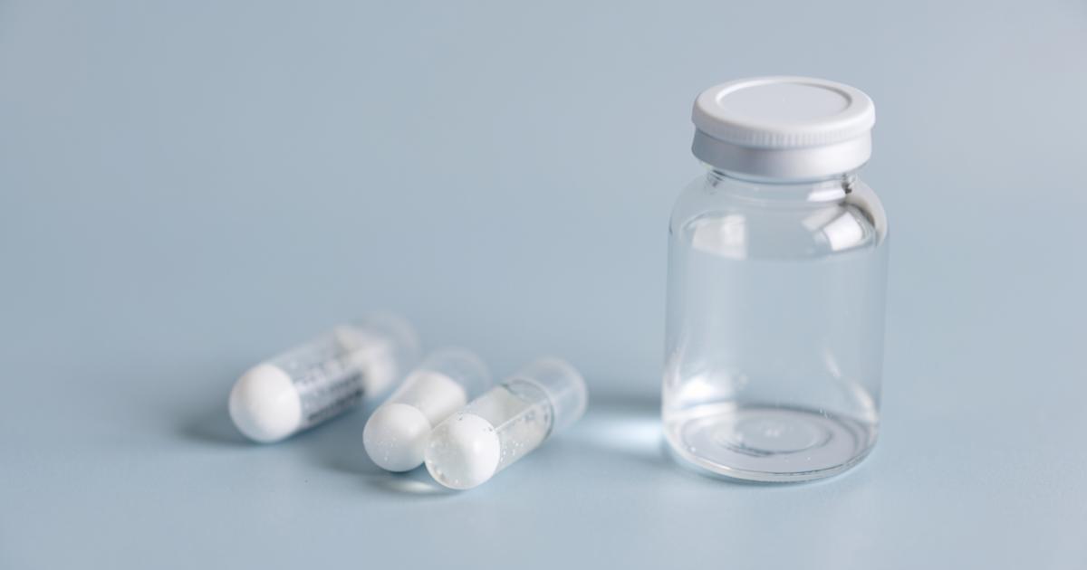Lyophilised powder vials beside a vial of sterile water on a blue-grey surface