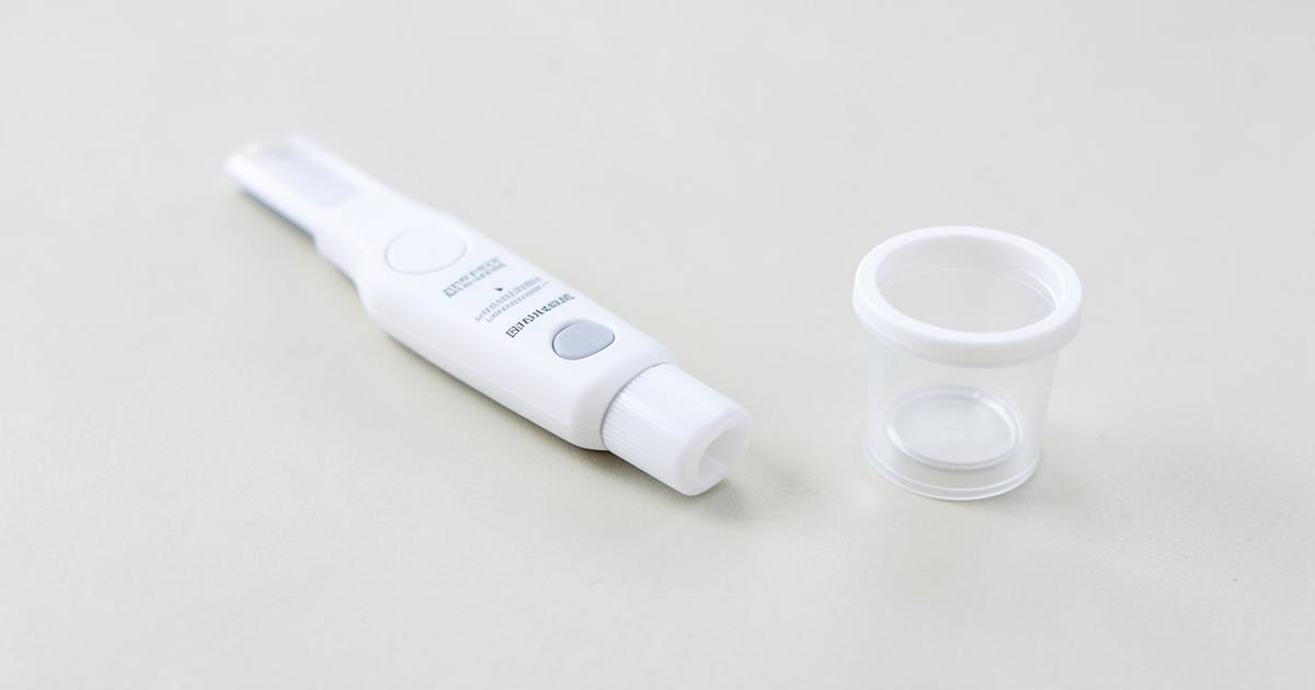 An unbranded white auto-injector pen on a pale surface beside a small container