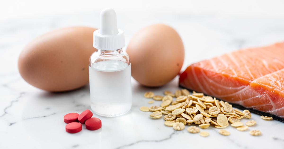 Vitamin B12 tablets and a sublingual spray beside eggs, salmon and fortified cereal on a marble surface