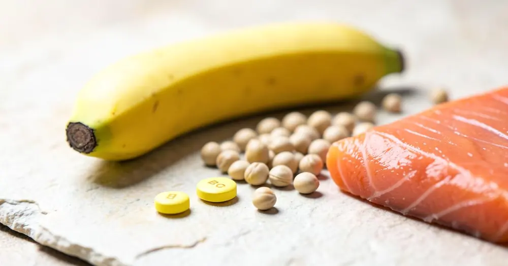 Yellow vitamin B6 tablets on a light stone surface beside a banana, chickpeas and salmon Yellow vitamin B6 tablets on a light stone surface beside a banana, chickpeas and salmon