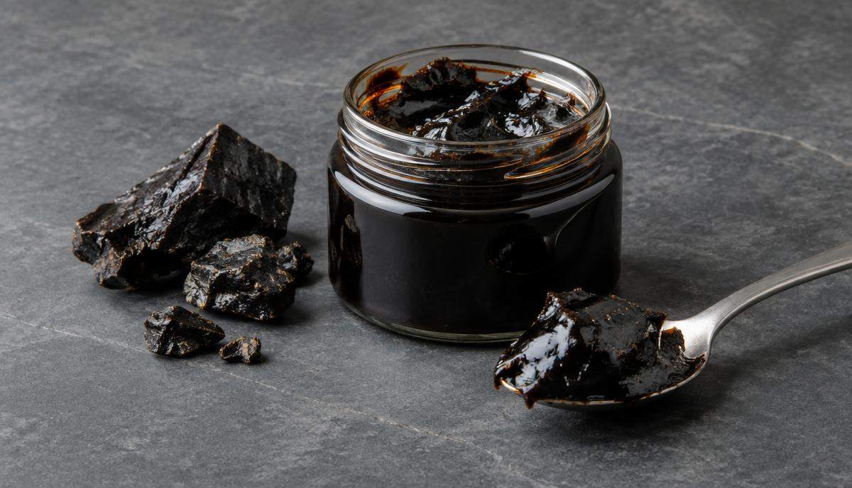 DoseRoutine Shilajit Dark resin in a small glass jar beside a spoon on stone